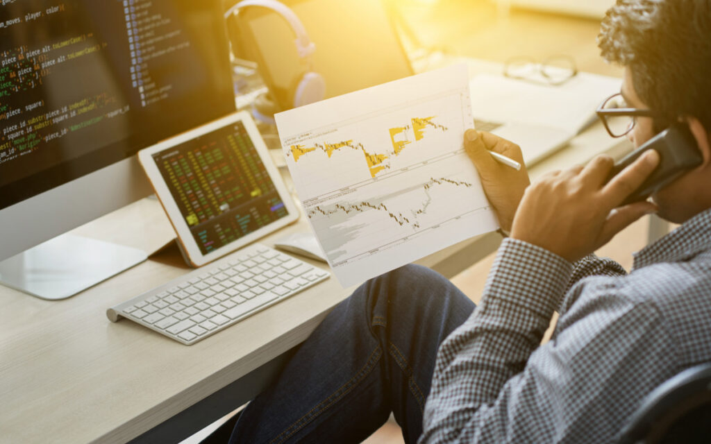 Man on phone in front of tablet and a graph on paper discussing the business value of IT.