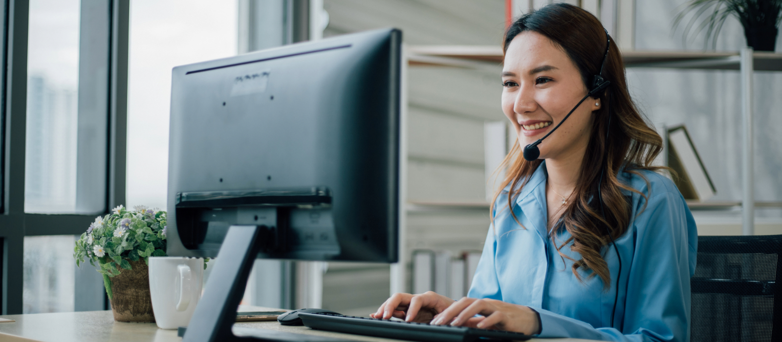 A woman with a headset in front of a computer providing help desk support.