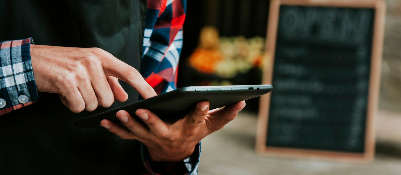 Small business owner standing in front of a chalkboard using a tablet, showing the advantages of digital transformation.