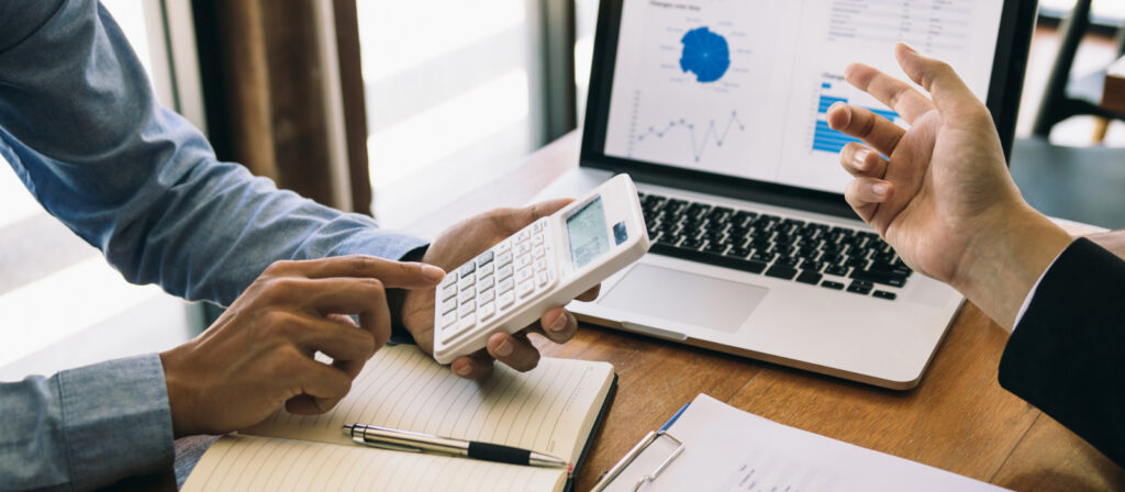 Two people discussing tariff prices while using a calculator and laptop on a desk.