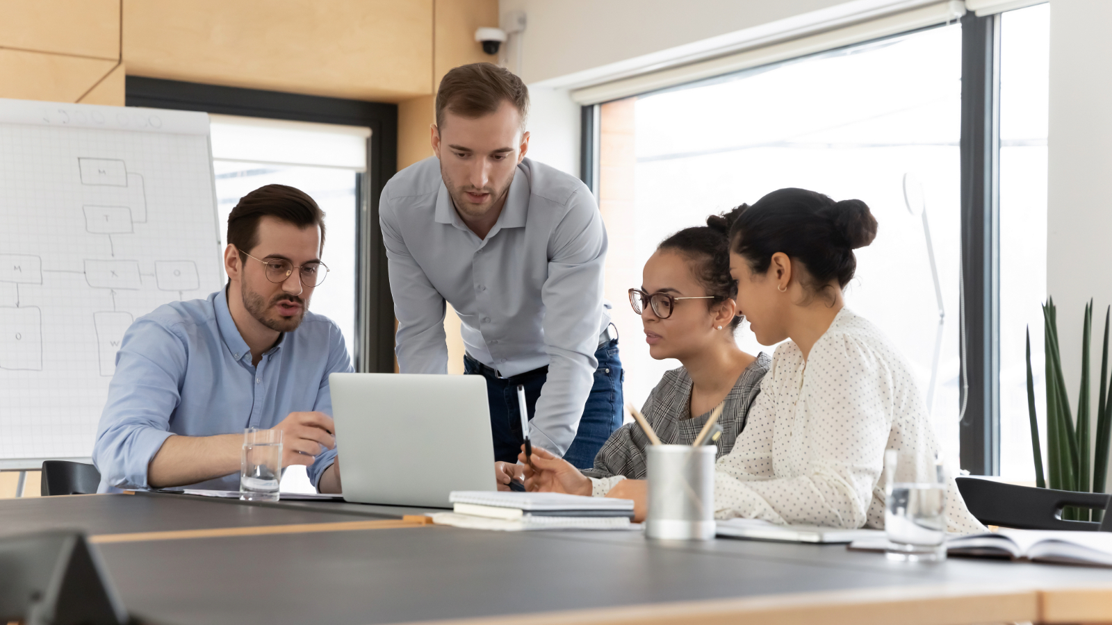 Four colleagues reviewing a laptop together in a modern office, representing collaboration between co-managed and in-house IT teams.