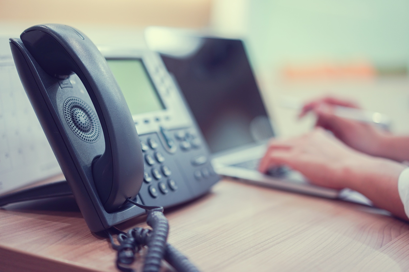 Close-up of an office desk showing a modern phone system next to a laptop, representing upgraded communication technology.