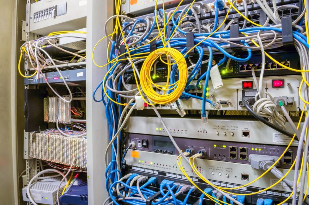 A close-up view of an old server rack filled with tangled network cables and outdated hardware, representing legacy IT systems that are difficult to manage and maintain.